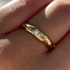 a woman's hand holding a gold ring with flowers on it and a diamond in the middle