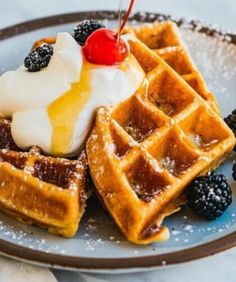 waffles with ice cream, berries and syrup on a blue plate topped with whipped cream