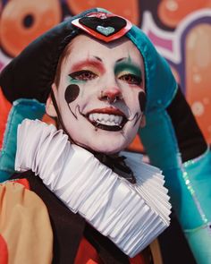 a man with clown makeup on his face and hands in the air, wearing gloves