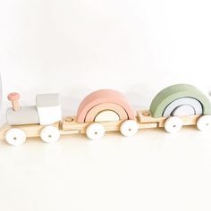 a wooden toy train with white wheels and pink, green, blue, yellow and orange colors