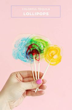 a hand holding three lollipops on a pink background with the text, colorful tequila lollipops