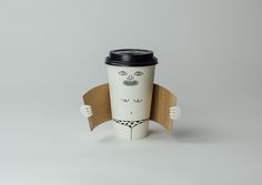 a coffee cup with a face drawn on it's side, holding up a cardboard cutout