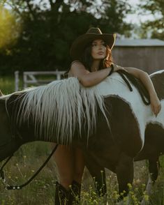 a woman wearing a cowboy hat sitting on top of a brown and white horse in a field