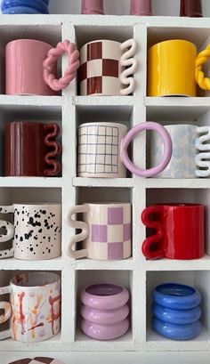 many different colored coffee cups are in a white box on the shelf next to each other