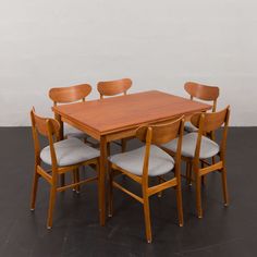 a wooden table with six chairs around it and a white wall in the back ground