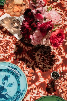 a table topped with plates and flowers on top of a red cloth covered tablecloth