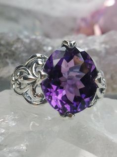 Natural Purple Amethyst RingSmall Fat Oval Design#D111 Inspired by Gothic designs, this stunning antique reproduction ring is crafted in sterling silver. This gorgeous ring is set with a flawless oval-cut natural purple amethyst. The stunning 3 carat weight gemstone is 11mm x 9mm. The band is marked 925 for sterling silver. Notice the beautiful silver filigree swirl setting and band. The bold style travels around the base of the gem and morphs into a solid band. The stunning gem rises above the Classic Oval Lavender Jewelry, Classic Lavender Oval Jewelry, Purple Amethyst Ring With Intricate Design, Elegant Purple Amethyst Ring With Intricate Design, Purple Promise Ring With Intricate Design, Purple Intricate Design Promise Ring, Elegant Sterling Silver Amethyst Ring Oval Cabochon, Classic Oval Cabochon Amethyst Jewelry, Exquisite Oval Purple Ring