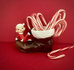 some candy canes are in a cup on a red tablecloth and there is a small figurine next to it