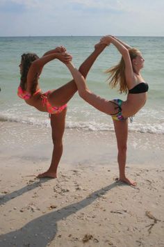 two women in bikinis doing yoga on the beach