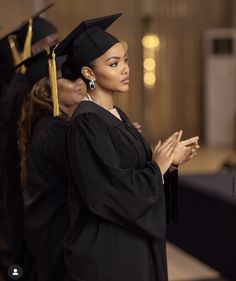 a woman standing in front of other people wearing graduation gowns and holding her hands together