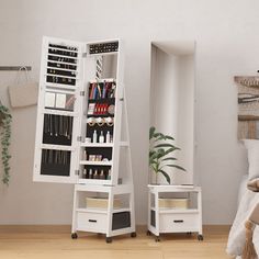 two white shelves with various items on them in the corner of a room next to a bed