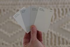 a hand holding four different shades of white paint