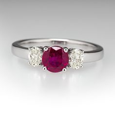 This pretty ring is centered with one (1) round mixed cut natural ruby set into a four-prong setting. The center stone is accented to each side by one (1) oval brilliant cut set into a four-prong setting. The ring measures 5.5mm at the top, rises 5.1mm above the finger, tapering to 2.2mm wide and 1.2mm thick at the base of the shank. This ring is currently a size 6.75. Formal Ruby Three Stone Ring With Diamonds, Elegant Three Stone Red Diamond Ring, Classic Diamond Ring With Lab-created Ruby Accent Stones, Elegant Three-stone Red Diamond Ring, Elegant Red Three Stone Diamond Ring, Elegant Red Three-stone Diamond Ring, Classic Three Stone Round Ruby Ring, Classic Three Stone Ruby Ring With Diamonds, Luxury Oval Three-stone Ruby Ring