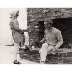 two people sitting on steps talking to each other in front of a brick building with a fire place