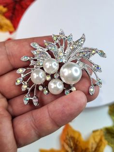 Add a touch of elegance to any outfit with this stunning Rhinestone Crystal and Pearl Flower Brooch Pin. The shining rhinestone crystals catch the light beautifully, reflecting different colors depending on the angle and creating a dazzling effect.  The brooch also features lustrous pearls and delicate flower petals made from high-quality materials, adding to its vintage-inspired charm. Measuring approximately 5.5cm in diameter, this brooch is the perfect size to wear on your lapel, blouse, dress, or scarf. Its silver color complements any outfit, making it ideal for special occasions such as weddings, engagements, parties, or evening wear. This Elegant Rhinestone Crystal and Pearl Flower Brooch Pin is not only a beautiful accessory for yourself but also makes a great Mother's Day gift for Formal White Rhinestone Brooches, Formal White Brooches With Rhinestones, White Rhinestone Brooches For Formal Occasions, Wedding Crystal Brooches With Sparkling Stones, Crystal Brooches With Rhinestones For Anniversary, Formal White Crystal Brooches, Elegant Silver Sparkling Brooches, Silver Jeweled Wedding Brooches, Silver Jeweled Brooch For Wedding