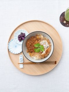 a bowl of food on a plate with chopsticks and a glass of green tea