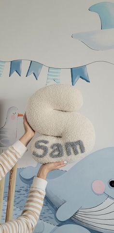 a woman is holding two pillows in front of a wall with an image of a whale