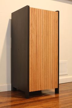 a wooden cabinet sitting on top of a hard wood floor next to a white wall