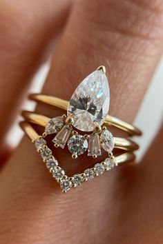 a woman's hand with two gold rings and a pear shaped diamond in the middle