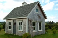 a small gray house with a ladder on the front door and windows that are open