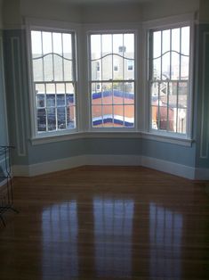 an empty room with three large windows and hard wood flooring on the far side