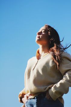 a woman with her eyes closed looking up into the sky while wearing a sweater and jeans