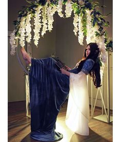 a woman sitting on top of a chair next to a flower covered arch with flowers hanging from it