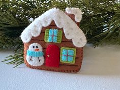 a gingerbread house ornament hanging from a christmas tree with snow on it