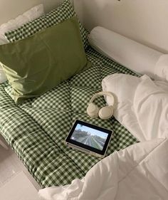 a laptop computer sitting on top of a green and white checkered comforter covered bed