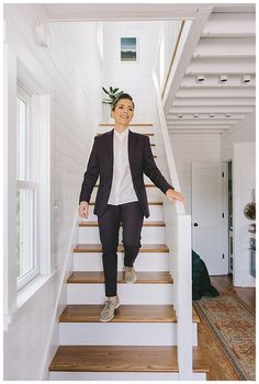 a woman in a suit standing on the stairs next to a door and potted plant