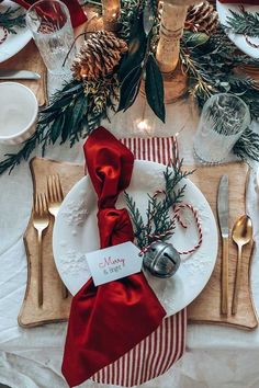 a place setting with pine cones, silverware and red ribbon on the napkins