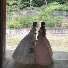 two women in dresses looking out the window