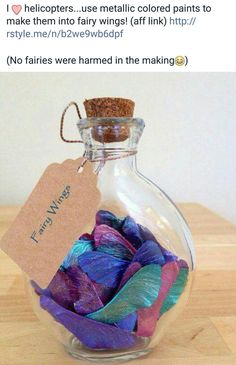 a glass bottle filled with purple and blue feathers on top of a wooden table next to a tag