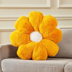 a yellow flower shaped pillow sitting on top of a gray couch next to a white wall