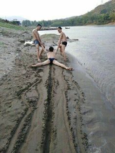 three men in bathing suits are on the beach and one man is laying on the ground