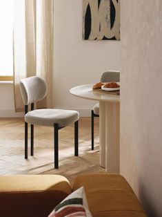 two chairs and a table in a room with white walls, wood flooring and paintings on the wall