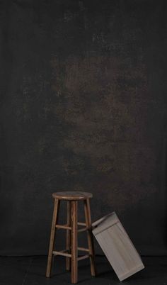 a wooden stool sitting in front of a black wall next to a piece of wood