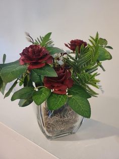 a vase filled with red flowers and green leaves