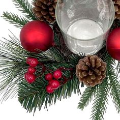 a glass filled with water surrounded by pine cones and red baubles on a white background