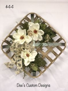 a white flower arrangement in a basket with ribbon on the bottom and green leaves around it