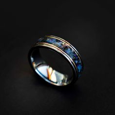 a wedding ring with blue and gold inlayed to it on a black surface