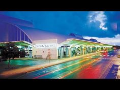 the building is lit up at night with colorful lights on it's sides and cars driving down the street