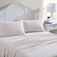 a white bed topped with two pillows next to a night stand and lamp on top of a dresser