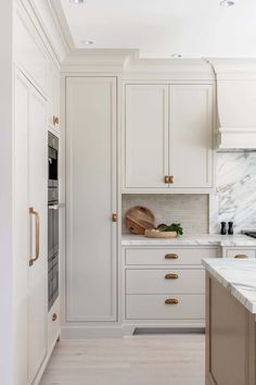 a kitchen with marble counter tops and white cabinets, along with brass pulls on the doors