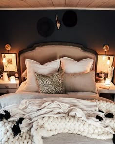 a bed with pillows and blankets on top of it next to two night stands filled with candles