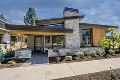 a modern home with stone and wood accents in the front yard, surrounded by landscaping