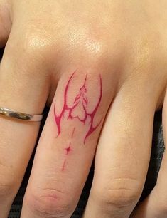 a woman's hand with a red ink tattoo on her left thumb and ring finger