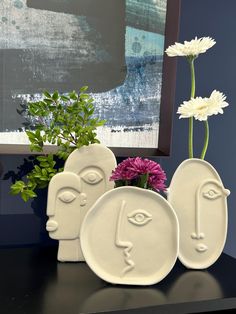 three white vases sitting on top of a black table next to a flower pot