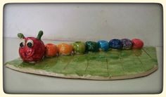 a ceramic figurine of a caterpillar on a leaf with seven different colors