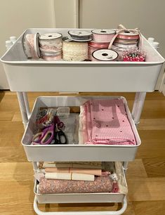 a white cart filled with lots of craft supplies on top of a hard wood floor